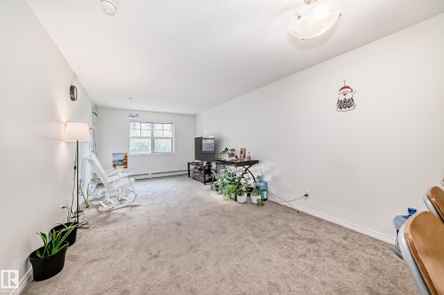 Spacious room featuring neutral carpeting, white wall finishes, and a multi-pane window - 113 11441 Ellerslie Road, Edmonton, AB - Indoor Photo Showing Other Room