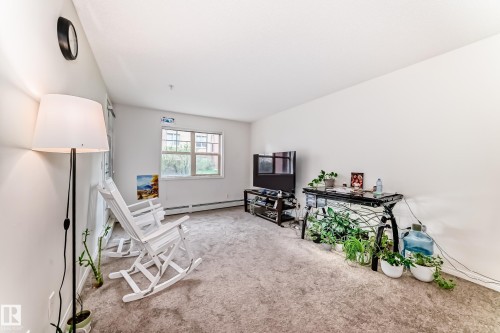 Living area with light-colored carpeting, white painted walls, and a large window - 113 11441 Ellerslie Road, Edmonton, AB - Indoor