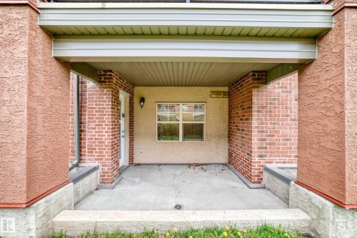 Covered patio area featuring a concrete surface, brick accents, stucco columns, and a beadboard ceiling - 113 11441 Ellerslie Road, Edmonton, AB - Outdoor With Exterior