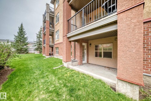 Ground-level patio with concrete flooring, featuring an exterior door and window set within the building's stucco and brick facade - 113 11441 Ellerslie Road, Edmonton, AB - Outdoor