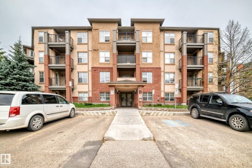 Multi-story residential building featuring a stucco and brick exterior, individual balconies with dark railings, multiple windows providing natural light, and a prominent ground-floor entrance with a covered overhang - 113 11441 Ellerslie Road, Edmonton, AB - Outdoor With Facade
