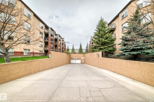 Concrete driveway leading to a security gate, flanked by textured stucco retaining walls - 113 11441 Ellerslie Road, Edmonton, AB - Outdoor