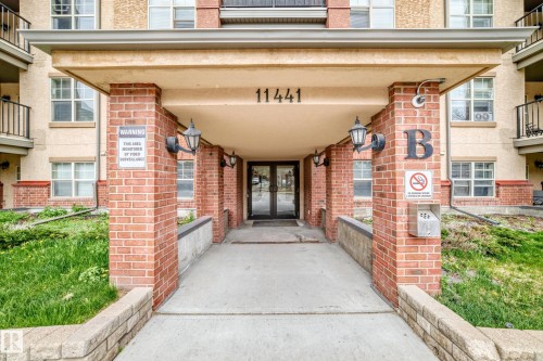 Covered entry featuring brick columns, exterior lighting fixtures, and concrete paving - 113 11441 Ellerslie Road, Edmonton, AB - Outdoor