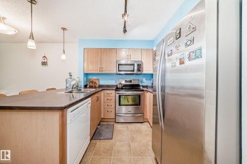 Kitchen featuring wood cabinetry, stainless steel appliances, a double basin sink, tile flooring, and a breakfast bar - 113 11441 Ellerslie Road, Edmonton, AB - Indoor Photo Showing Kitchen