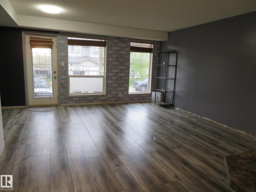 Spacious interior featuring wood-finish flooring, accent wall with brick-patterned finish, large windows, and a glass-paneled door - 2945 26 Street, Edmonton, AB - Indoor Photo Showing Other Room