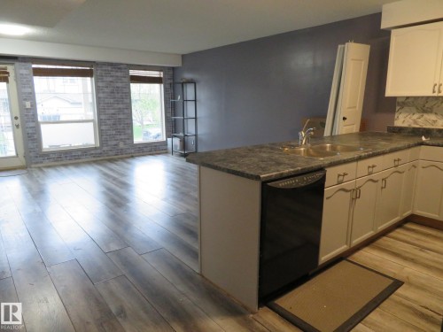 Open concept area featuring wood-finish flooring, a kitchen island with a double basin sink, and a black dishwasher - 2945 26 Street, Edmonton, AB - Indoor Photo Showing Kitchen With Double Sink
