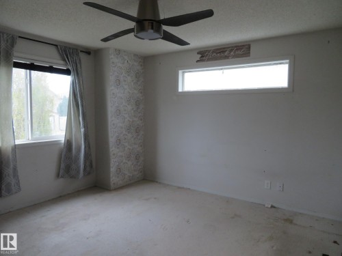 Spacious room featuring a ceiling fan with integrated lighting, two window openings, and a decorative accent wall with patterned wallpaper - 2945 26 Street, Edmonton, AB - Indoor