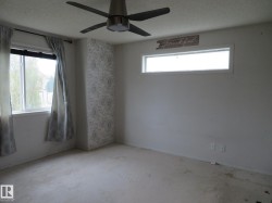 Spacious room featuring a ceiling fan with integrated lighting, two window openings, and a decorative accent wall with patterned wallpaper - 