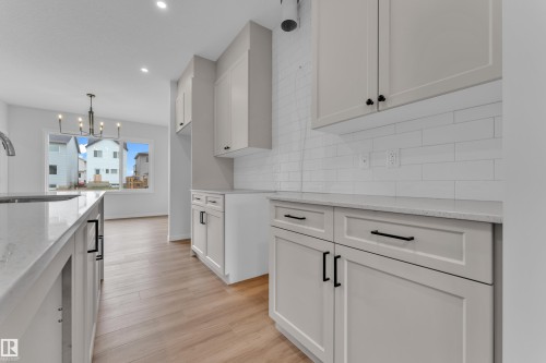 Modern kitchen featuring light wood-finish flooring, white shaker-style cabinetry with matte black hardware, white subway tile backsplash, and light-toned countertops - 17330 6A Street Ne, Edmonton, AB - Indoor Photo Showing Kitchen