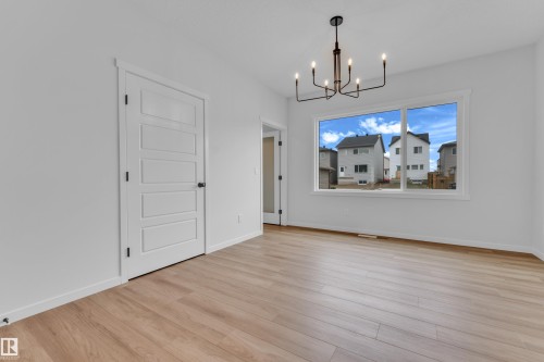 Open room featuring wood-finish flooring, white baseboards, a large window, and a contemporary black chandelier - 17330 6A Street Ne, Edmonton, AB - Indoor