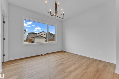 Bright interior room featuring a multi-pane window, wood-finish flooring, a contemporary chandelier, and a white trim package - 17330 6A Street Ne, Edmonton, AB - Indoor Photo Showing Other Room