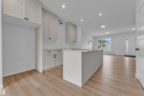 Modern kitchen featuring a central island with a sink and chrome faucet, light grey cabinetry with black hardware, white subway tile backsplash, recessed lighting, and wood-finish flooring - 17330 6A Street Ne, Edmonton, AB - Indoor Photo Showing Kitchen