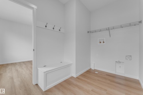 Bright utility area featuring wood-finish flooring, a built-in storage bench with coat hooks, and laundry hookups - 17330 6A Street Ne, Edmonton, AB - Indoor