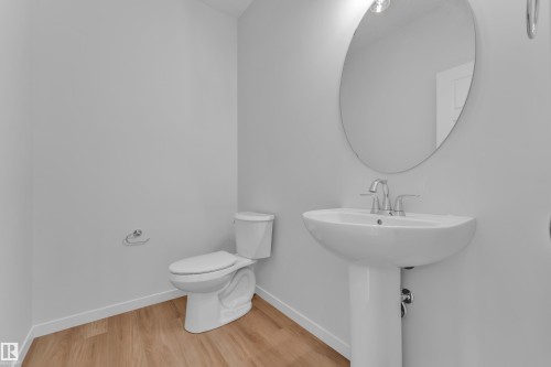 Bathroom featuring a pedestal sink with a chrome faucet, oval mirror, and wood-finish flooring - 17330 6A Street Ne, Edmonton, AB - Indoor Photo Showing Bathroom