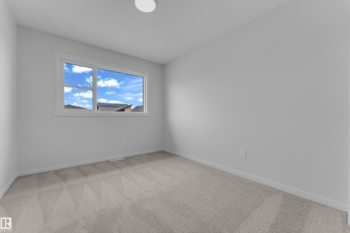 Bright interior space featuring a window with white trim, light gray carpet, white walls, white baseboards, and a flush-mount ceiling light - 17330 6A Street Ne, Edmonton, AB - Indoor Photo Showing Other Room