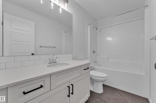 Bathroom featuring a single vanity with a light-toned countertop, white cabinetry with black hardware, a rectangular mirror, and a combination tub and shower with white subway tile surround - 17330 6A Street Ne, Edmonton, AB - Indoor Photo Showing Bathroom