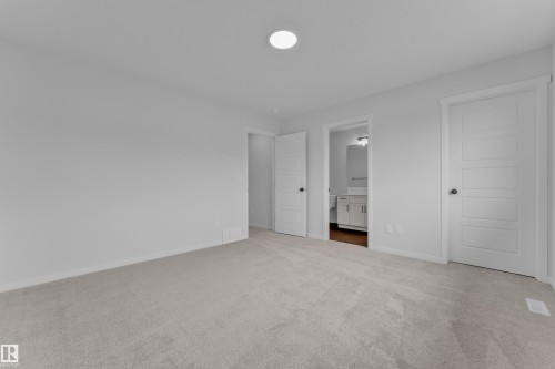 Carpeted room featuring light gray walls, a flush-mount ceiling light, and two white paneled doors with dark hardware - 17330 6A Street Ne, Edmonton, AB - Indoor Photo Showing Other Room