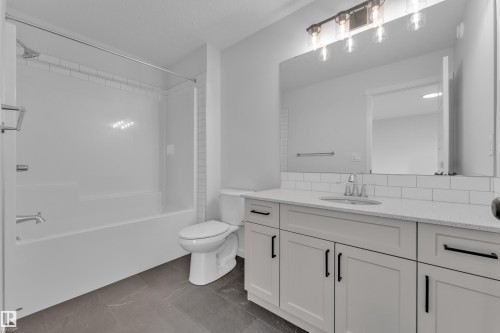 Full bathroom featuring a single vanity with stone-finish countertop, white cabinetry with matte black hardware, integrated sink, and a combination shower and bathtub with white subway tile surround - 17330 6A Street Ne, Edmonton, AB - Indoor Photo Showing Bathroom