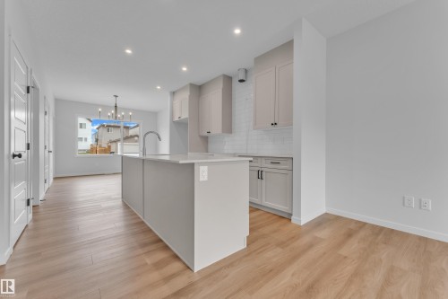 Open-concept kitchen featuring a central island with an integrated sink, light-toned cabinetry, subway tile backsplash, recessed lighting, and wood-finish flooring - 17330 6A Street Ne, Edmonton, AB - Indoor Photo Showing Kitchen