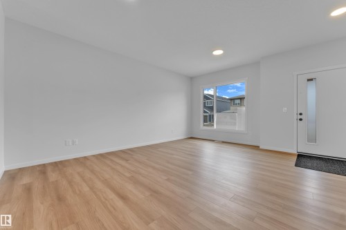 Spacious entry area featuring wood-finish flooring, recessed lighting, a white entry door with a frosted glass insert, and a large window providing natural light - 17330 6A Street Ne, Edmonton, AB - Indoor Photo Showing Other Room