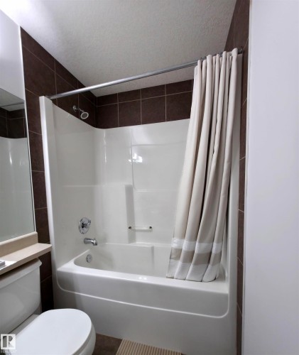White acrylic bathtub and shower combination featuring chrome fixtures and brown tiled surround - 210 5005 165 Avenue, Edmonton, AB - Indoor Photo Showing Bathroom