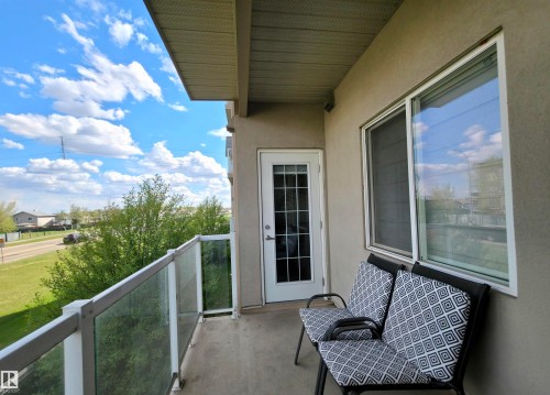 Private balcony featuring a glass railing system, stucco exterior, and a white framed window - 210 5005 165 Avenue, Edmonton, AB - Outdoor With Balcony With Exterior