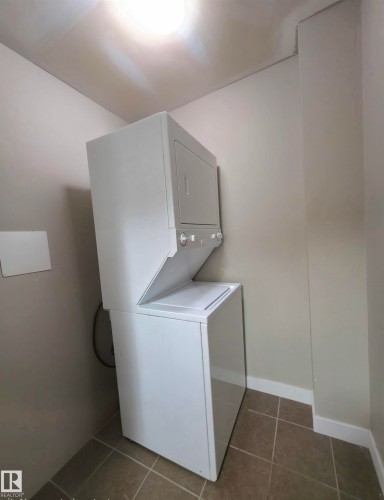 Dedicated laundry area featuring a white stacked washer and dryer unit, neutral wall paint, white baseboards, and tile flooring - 210 5005 165 Avenue, Edmonton, AB - Indoor Photo Showing Laundry Room