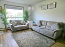 Bright living area featuring a large window, light wood-finish flooring, and a textured area rug - 210 5005 165 Avenue, Edmonton, AB  - Indoor Photo Showing Living Room 