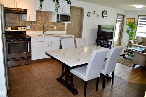 Open-concept living area featuring a kitchen with white cabinetry, stainless steel appliances, and a tiled backsplash - 210 5005 165 Avenue, Edmonton, AB - Indoor