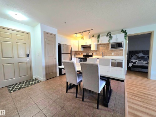 Open-concept kitchen and dining area featuring white cabinetry, stainless steel appliances, and a tiled backsplash - 210 5005 165 Avenue, Edmonton, AB - Indoor Photo Showing Other Room