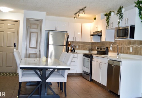 Contemporary kitchen featuring white cabinetry, stainless steel appliances, and a tiled backsplash - 210 5005 165 Avenue, Edmonton, AB - Indoor Photo Showing Kitchen With Stainless Steel Kitchen