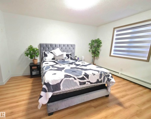 Bright room featuring wood-finish flooring, white walls, and a window with horizontal blinds and a brown frame - 210 5005 165 Avenue, Edmonton, AB - Indoor Photo Showing Bedroom