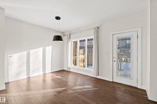 Spacious room featuring wood-finish flooring, a contemporary pendant light fixture, and a large multi-pane window - 2036 Ainslie Link Link, Edmonton, AB - Indoor Photo Showing Other Room