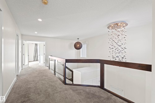 Upper-level hallway featuring a contemporary chandelier, recessed lighting, and a glass panel railing with a dark wood-finish top rail - 2036 Ainslie Link Link, Edmonton, AB - Indoor Photo Showing Other Room