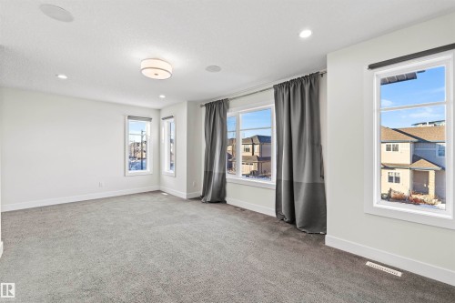 Spacious room featuring light gray carpeting, multiple large windows with white trim, and a contemporary ceiling light fixture - 2036 Ainslie Link Link, Edmonton, AB - Indoor Photo Showing Other Room