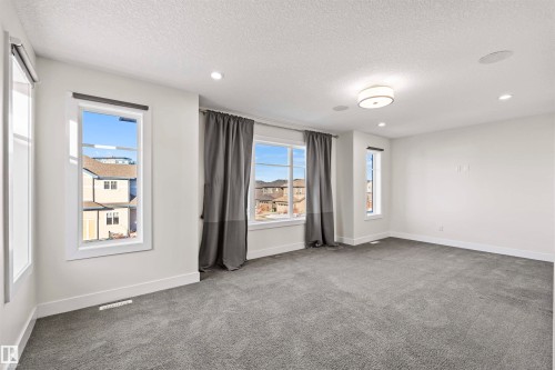Spacious room featuring light gray carpeting, multiple windows, a ceiling-mounted light fixture, recessed lighting, and integrated ceiling speakers - 2036 Ainslie Link Link, Edmonton, AB - Indoor Photo Showing Other Room