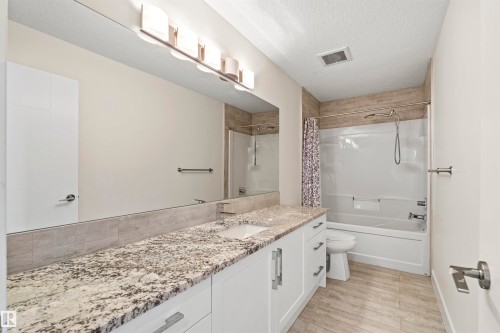 Bathroom featuring a long vanity with stone countertop, undermount sink, and white cabinetry - 2036 Ainslie Link Link, Edmonton, AB - Indoor Photo Showing Bathroom