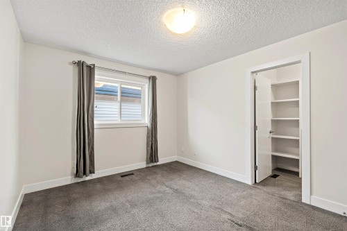 Carpeted room featuring a double-pane window with dark drapes, white baseboards, and a built-in closet with shelving - 2036 Ainslie Link Link, Edmonton, AB - Indoor Photo Showing Other Room