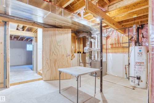 Unfinished basement space featuring exposed wood joists and structural beams, a visible water heater and furnace, and concrete flooring - 2036 Ainslie Link Link, Edmonton, AB - Indoor Photo Showing Basement