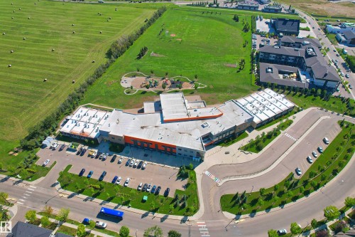 Modern building structure featuring a large parking area, expansive green spaces, and a playground - 2036 Ainslie Link Link, Edmonton, AB - Outdoor With View