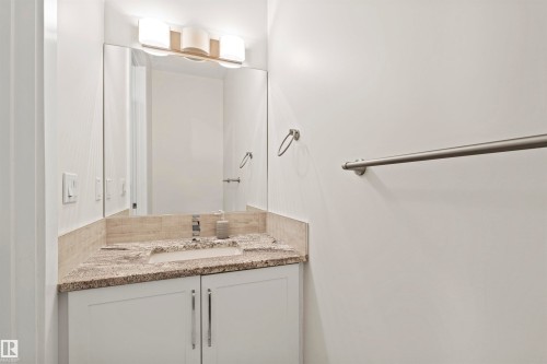 Vanity area featuring a built-in sink with a single-handle faucet, stone countertop, white cabinetry with metal pulls, and a large wall-mounted mirror - 2036 Ainslie Link Link, Edmonton, AB - Indoor Photo Showing Bathroom