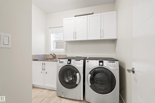 Dedicated laundry space featuring white shaker cabinetry, granite-style countertop, and a stainless steel sink - 2036 Ainslie Link Link, Edmonton, AB - Indoor Photo Showing Laundry Room