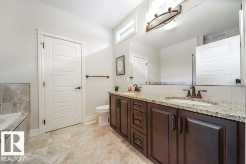 Bathroom featuring a dual-sink vanity with a granite-finish countertop, dark wood-finish cabinetry, and contemporary bronze-tone fixtures - 3 8050 Orchards Green, Edmonton, AB - Indoor Photo Showing Bathroom