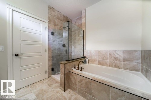 Bathroom featuring a walk-in shower with clear glass enclosure, tile surround, and built-in bench - 3 8050 Orchards Green, Edmonton, AB - Indoor Photo Showing Bathroom