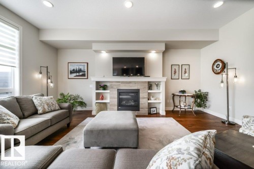 Living area featuring a gas fireplace with a stone surround, a white mantel, and built-in shelving - 3 8050 Orchards Green, Edmonton, AB - Indoor Photo Showing Living Room With Fireplace