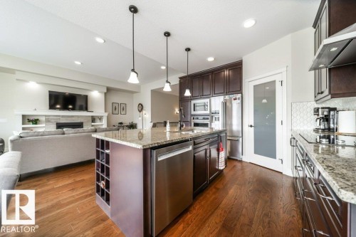 Kitchen island with granite countertop, integrated wine rack, and stainless steel dishwasher - 3 8050 Orchards Green, Edmonton, AB - Indoor Photo Showing Kitchen With Upgraded Kitchen