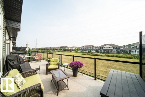 Spacious outdoor deck featuring a glass and black metal railing, offering expansive views of open green space - 3 8050 Orchards Green, Edmonton, AB - Outdoor With Deck Patio Veranda