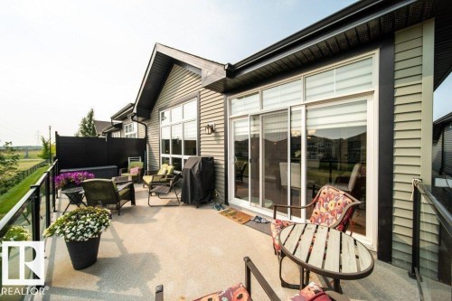 Expansive concrete patio featuring a glass and metal railing, privacy screen, and direct access to interior via sliding glass doors - 3 8050 Orchards Green, Edmonton, AB - Outdoor With Deck Patio Veranda