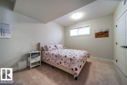 Carpeted interior room featuring a single window with blinds, a flush-mount ceiling light, and white paneled doors with dark hardware - 3 8050 Orchards Green, Edmonton, AB - Indoor Photo Showing Bedroom