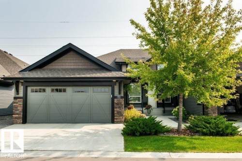 Contemporary residential exterior featuring a two-car garage with panel detailing, stone column accents, and a shingled roof - 3 8050 Orchards Green, Edmonton, AB - Outdoor
